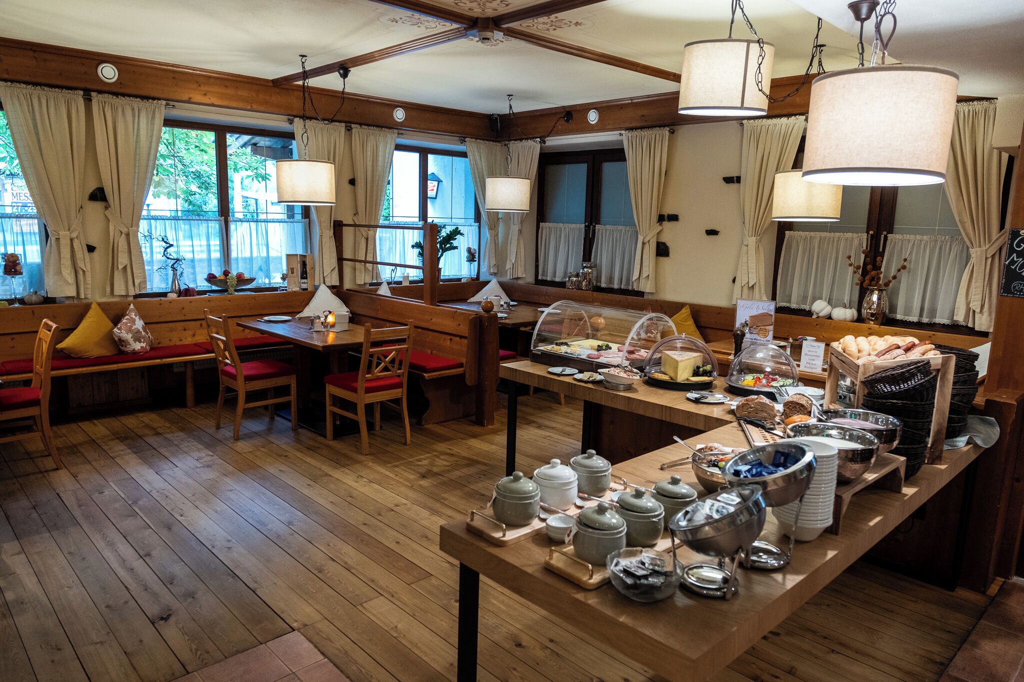 Un comedor acogedor con muebles de madera, una mesa de buffet con alimentos y ventanas amplias con cortinas.