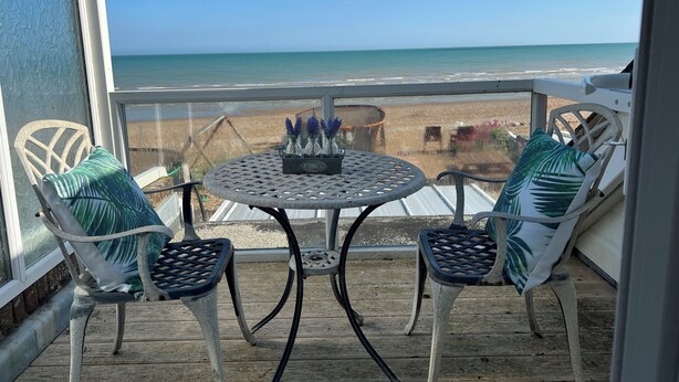 Ein Balkon mit rundem Tisch und zwei Stühlen, mit Blick auf einen Strand.