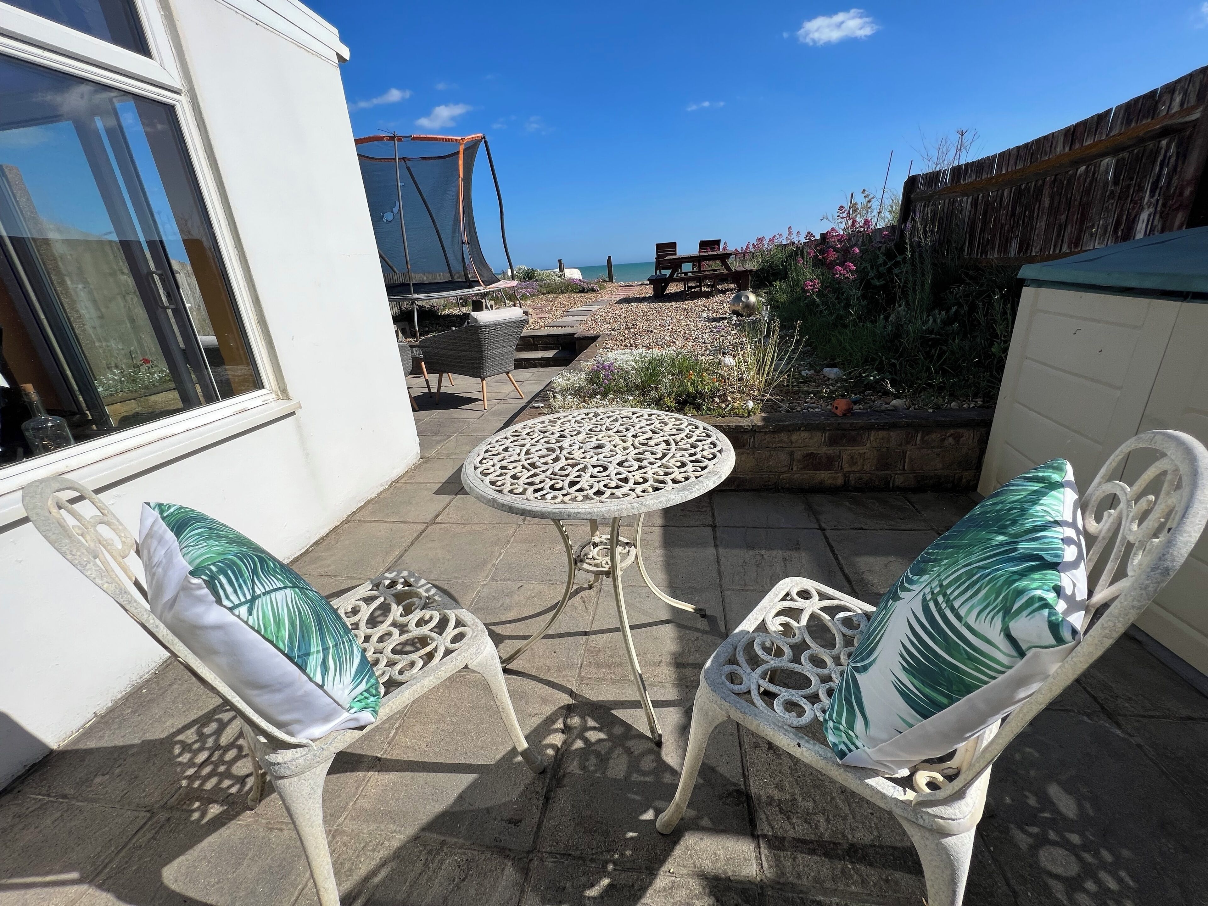 A patio with two chairs and a table, a wooden fence, and a view of the sea.