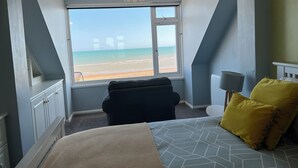 Ein Schlafzimmer mit Bett, Sessel, Fenster und Meerblick sowie einer Lampe.