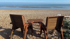 Eine hölzerne Bank und ein Tisch an einem Kiesstrand mit Blick auf das Meer.