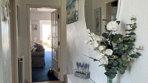 Ein Flur mit einem gemusterten Teppich, einem weißen Beistelltisch mit Spiegel, einer Vase mit Blumen und einer Tür, die in einen anderen Raum führt.