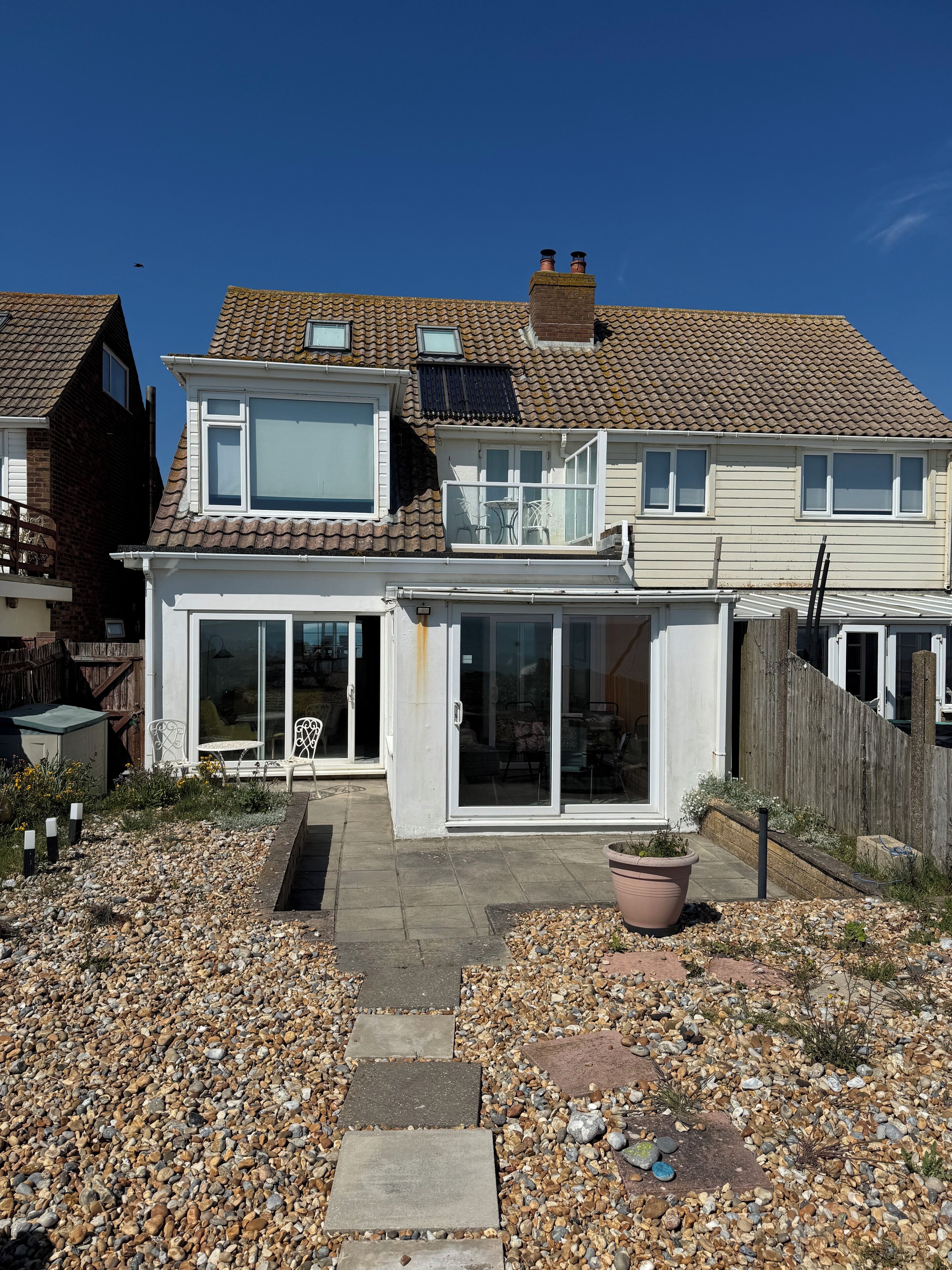 A two-story house with a patio, a large sliding glass door, and a small garden area with pebbles and a potted plant.