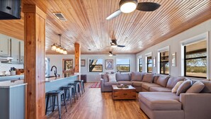 Un vaste espace de vie doté d’un plafond en bois, d’un grand canapé d’angle et d’une cuisine avec des tabourets de bar.