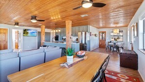 Un vaste espace de vie doté d’un plafond en bois, d’une table à manger et d’une cuisine située à l’arrière-plan.