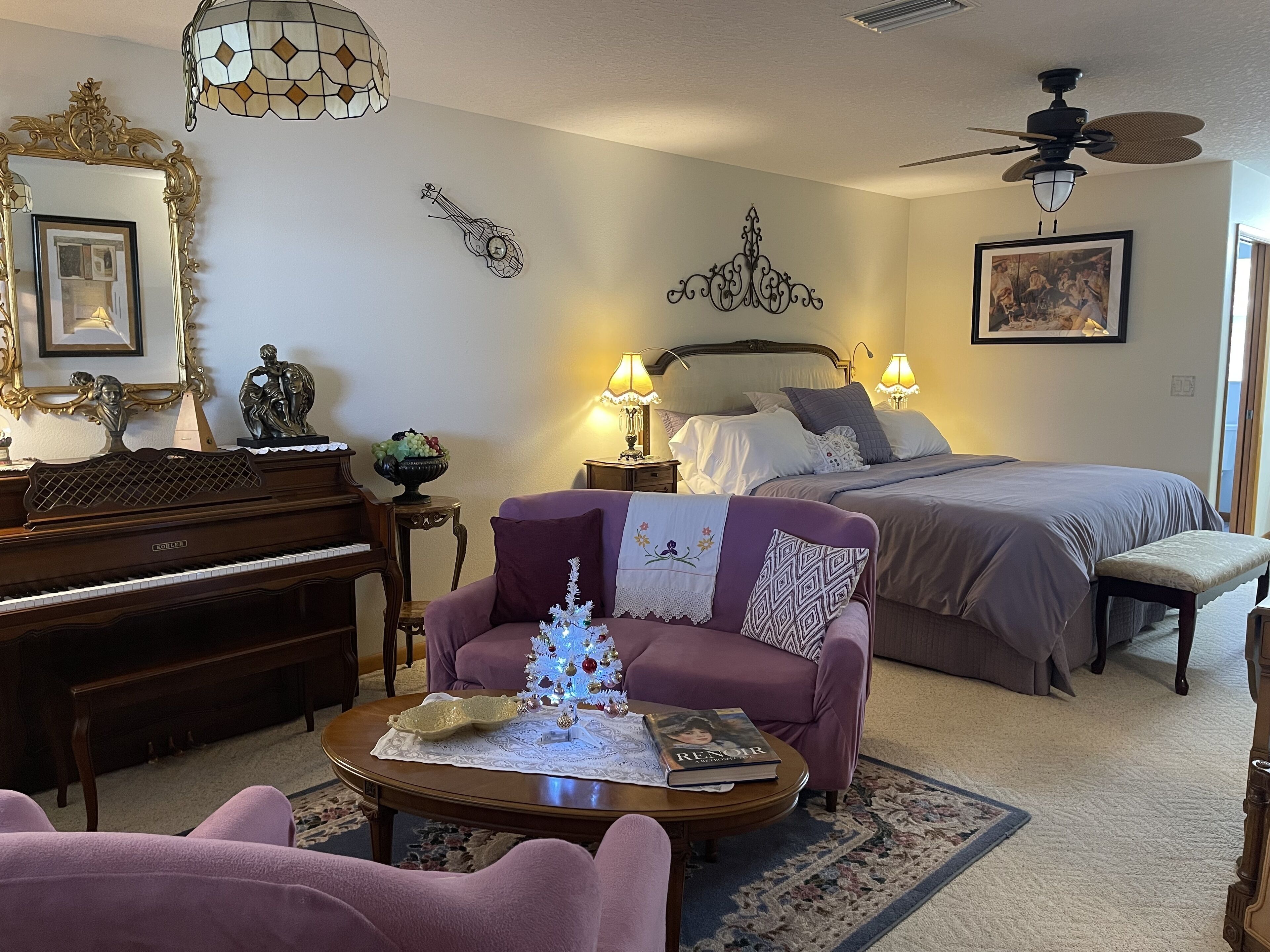Ein gemütliches Schlafzimmer mit einem Bett, Nachttischlampen, einem Klavier, einem kleinen Weihnachtsbaum und einem Wandkunstwerk.