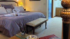 Habitación de hotel con cama, escritorio con lámpara, ventilador de techo y un cuadro en la pared.