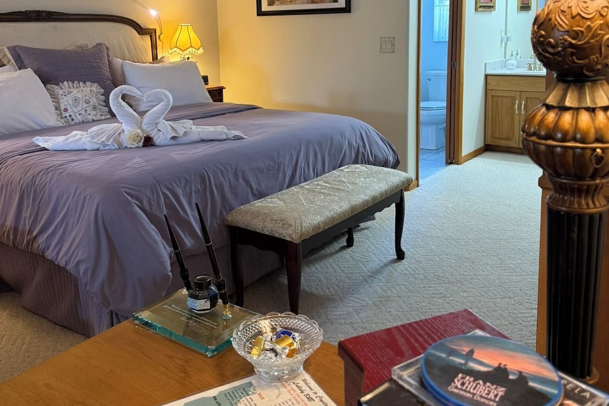 Une chambre d’hôtel avec un lit, un bureau doté d’une lampe, un ventilateur de plafond et un tableau encadré au mur.