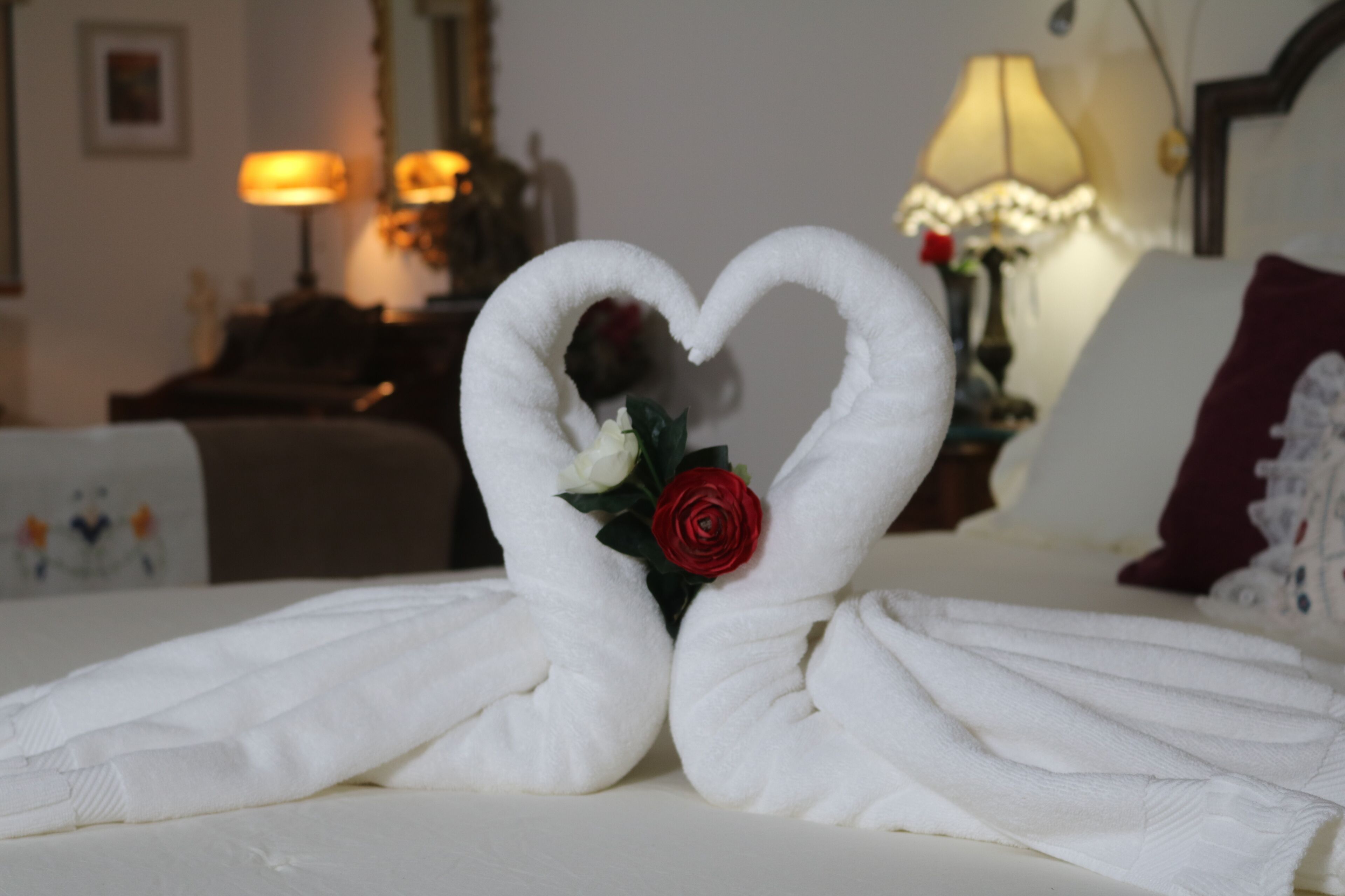 Una cama con una toalla dispuesta en forma de corazón y una rosa roja.
