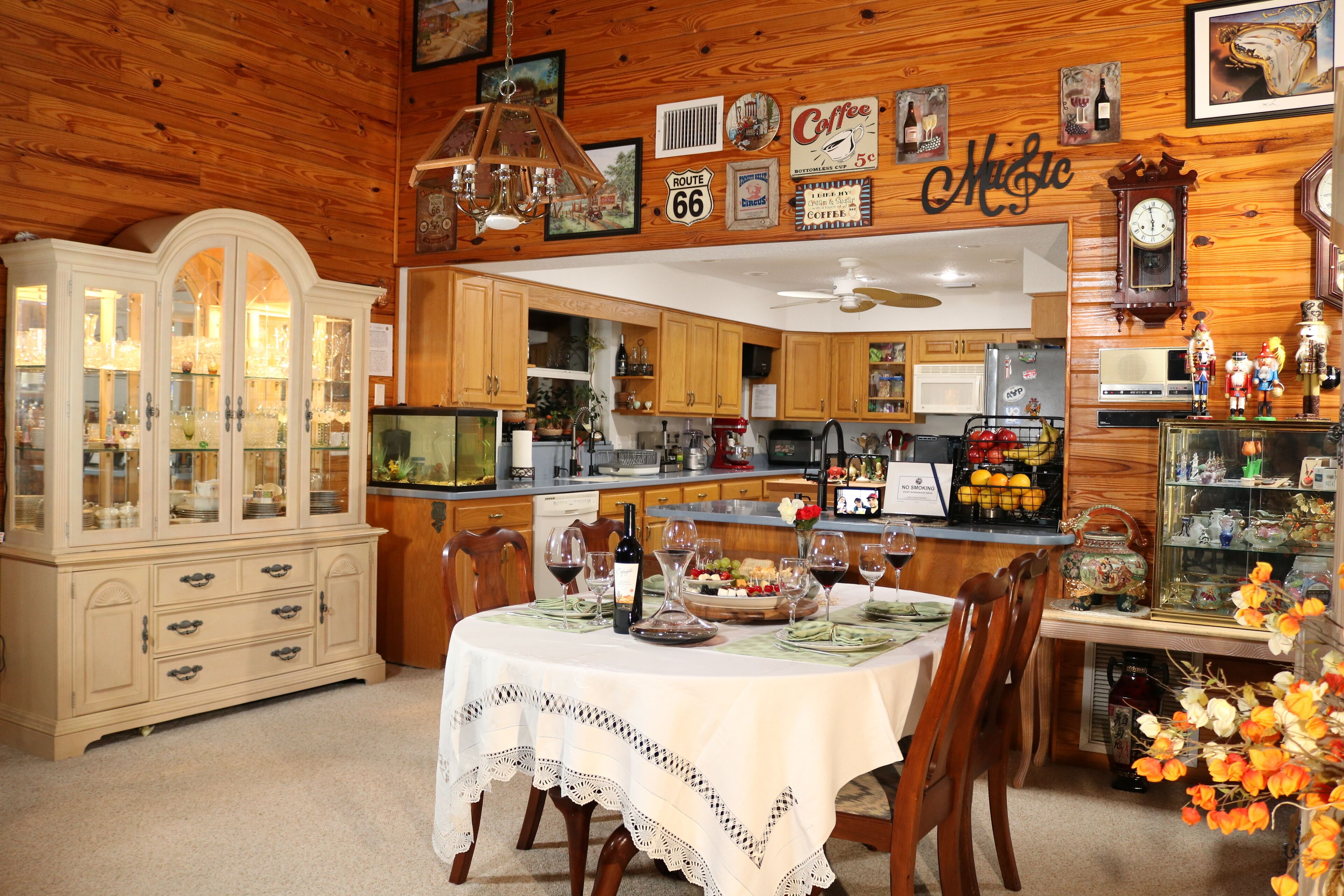 Un interior de madera con una mesa de comedor dispuesta para una comida, armarios de madera, una zona de cocina y diversos objetos decorativos.