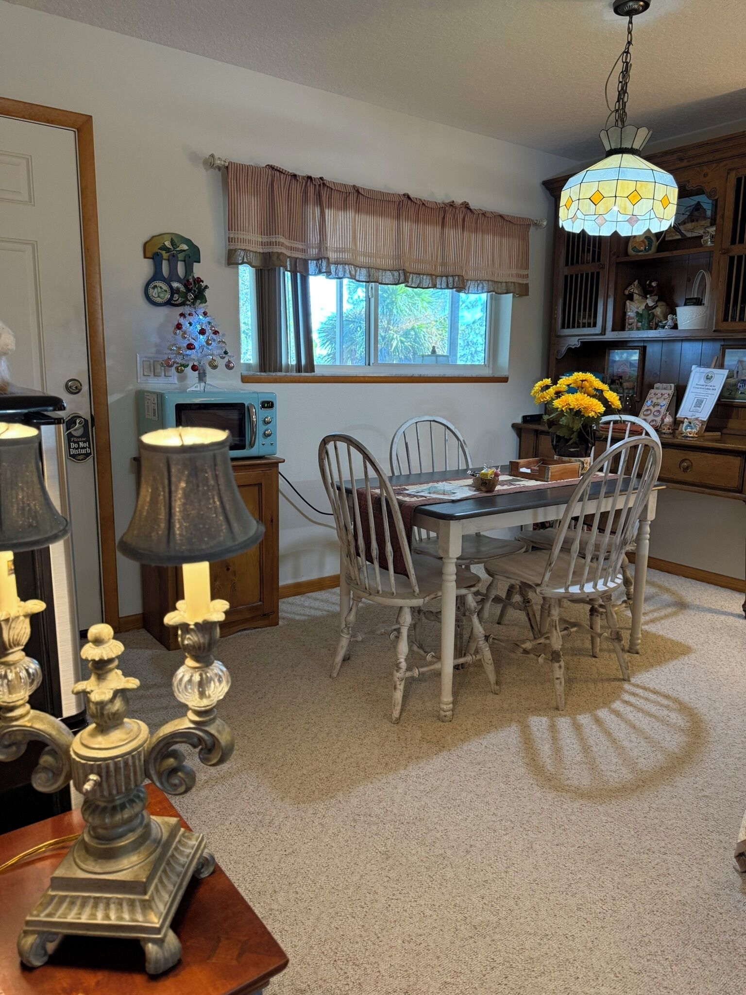 A dining area with a table, chairs, a chandelier, and a window with curtains.