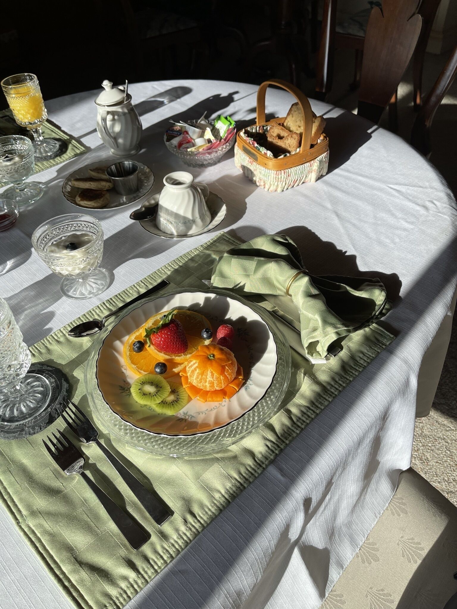 Uma mesa de café da manhã com uma travessa de frutas, um bule e diversos itens para o café.