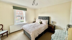 Een slaapkamer met een groot bed, een raam met uitzicht op gebouwen, een radiator, een stoel, een nachtkastje met een lamp en een garderobe.
