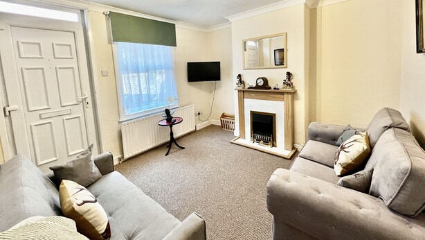 Een woonkamer met een open haard, een aan de muur bevestigde televisie en een groot raam met uitzicht op de omgeving.