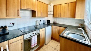 Een keuken met houten kastjes, een zwart aanrecht, een roestvrijstalen spoelbak, een witte waterkoker, een broodrooster en een vaatwasser.
