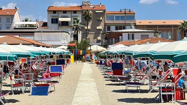 Un paseo marítimo con hileras de sillas de playa y sombrillas, un cielo despejado y edificios al fondo.