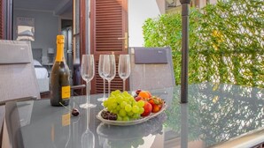 Una mesa con una botella de champán, cuatro copas y un plato de uvas y fruta.