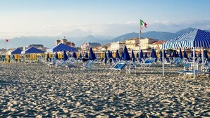 Una playa con hileras de sombrillas y tumbonas a rayas azules y blancas.