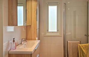 A modern bathroom with a glass shower enclosure, a wooden vanity, and a window above the sink.