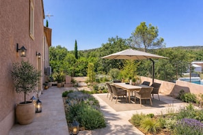 A patio with a table and chairs, surrounded by potted plants and a view of a pool.