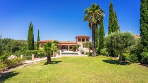 A Mediterranean-style villa with a central courtyard, surrounded by well-maintained gardens and tall cypress trees.