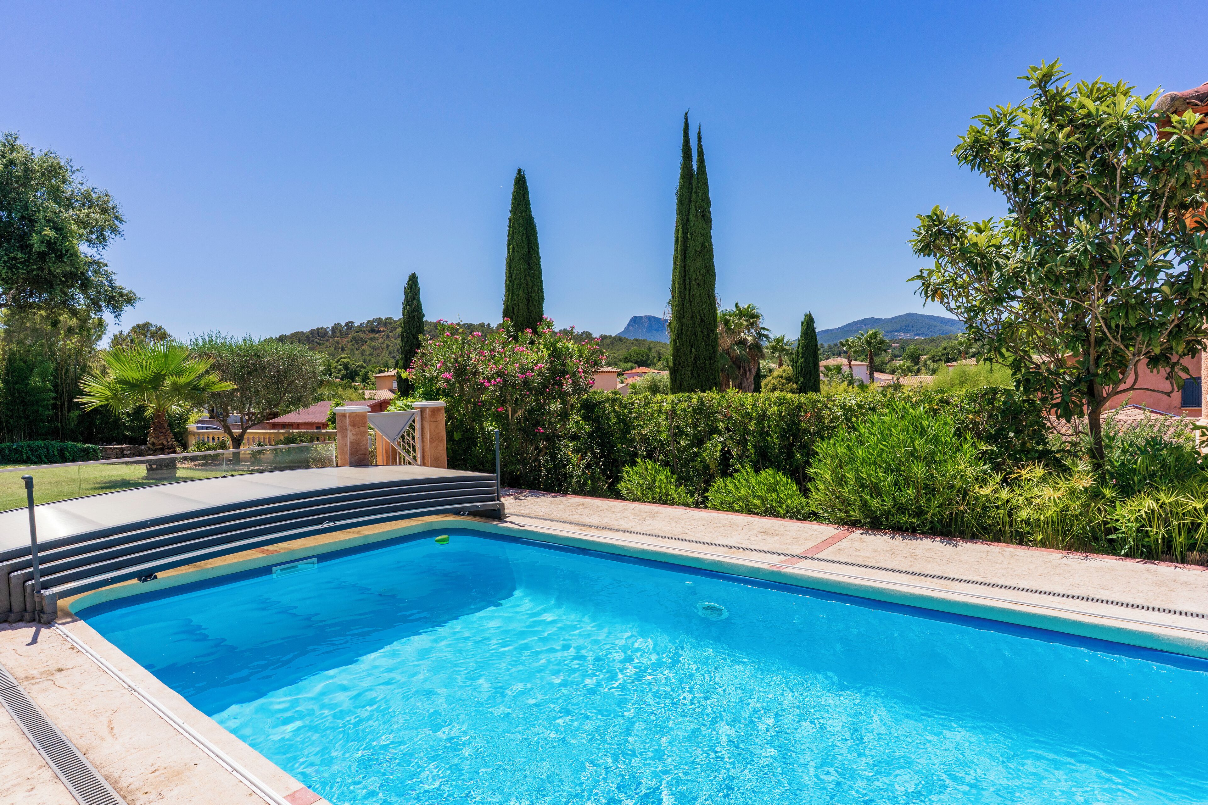A rectangular swimming pool with steps leading into it, surrounded by greenery and a clear sky.