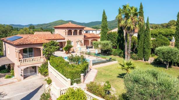 A large villa with a swimming pool, multiple balconies, and a lush garden.