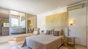 A modern bedroom with a large bed, a bathroom visible through a sliding door, and a large mirror.