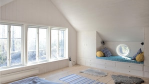 Een kamer met een schuine plafond, grote ramen, een inbouwbank met kussens en een rond dakvenster.