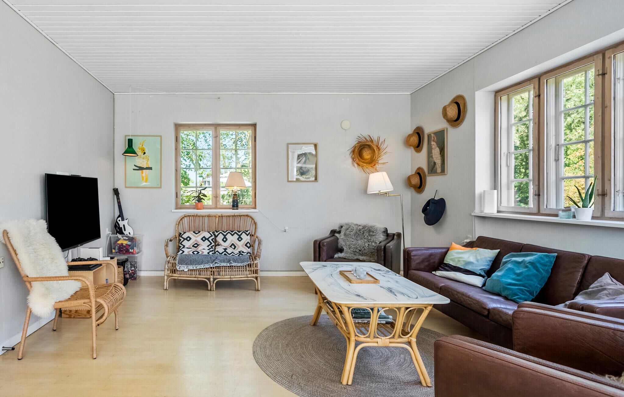 Ett mysigt vardagsrum med en tv, möbler i rotting, en brun lädersoffa och ett matbord.