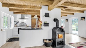 Une cuisine moderne dotée d’un îlot central, de poutres apparentes en bois au plafond et d’un poêle à bois.