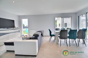 A modern living room with a flat-screen TV, a sofa, and a dining area with chairs and a table.