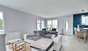 A modern living room with a sofa, coffee table, and dining area. - La Villa de L'océan - Erdeven (ERDEVEN)