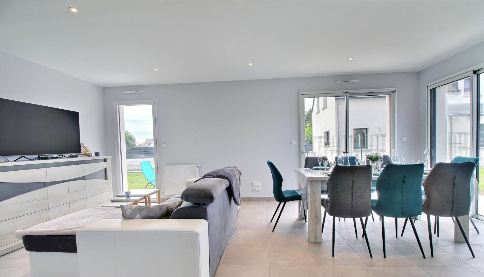 A modern living room with a flat-screen TV, a sofa, and a dining area with chairs and a table.