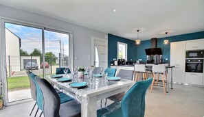 A modern kitchen with a central island, a dining area with a glass table, and a view of the outside. - La Villa de L'océan - Erdeven (ERDEVEN)