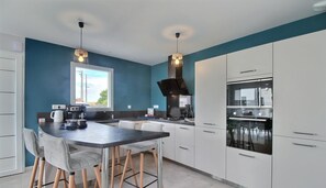 A modern kitchen with white cabinets, a black countertop, and a built-in oven. There is a window providing natural light and a view of the outside. - La Villa de L'océan - Erdeven (ERDEVEN)