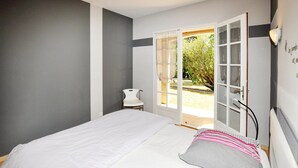 A bedroom with a bed, a small white chair, and a door leading to an outdoor area. - Lovely home in Limoux (Limoux)