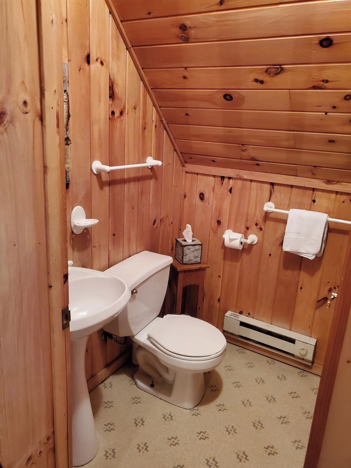 A wooden-paneled bathroom with a toilet, sink, and towel rack.