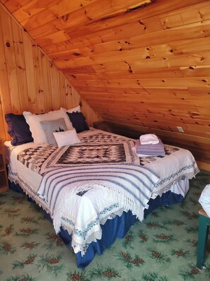 Ein Schlafzimmer mit schrägverlegtem Holzboden, einem Bett mit einem gemusterten Bettdeckbett und einem grünen floralen Teppich.