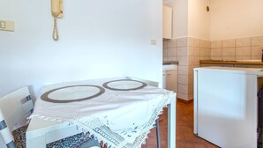 A dining table with a white tablecloth and two circular placemats, a white refrigerator, and a kitchen area with tiled walls and a stove. - Lovely apartment in Portoroz with house sea view (Portoroz)