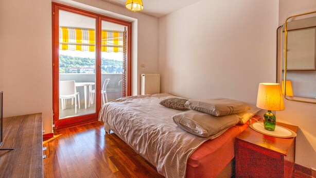 A bedroom with a bed, a nightstand, a lamp, a radiator, and a sliding glass door leading to a balcony. - Lovely apartment in Portoroz with house sea view (Portoroz)