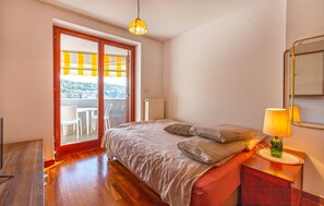 Ein Schlafzimmer mit einem Bett, einem Nachttisch, einer Lampe, einer Heizung und einer Glastür, die auf einen Balkon führt.