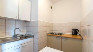 A compact kitchen with a sink, stove, and kettle, featuring white cabinets and beige tiles. - Lovely apartment in Portoroz with house sea view (Portoroz)