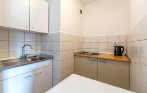 A compact kitchen with a sink, stove, and kettle, featuring white cabinets and beige tiles. - Lovely apartment in Portoroz with house sea view (Portoroz)