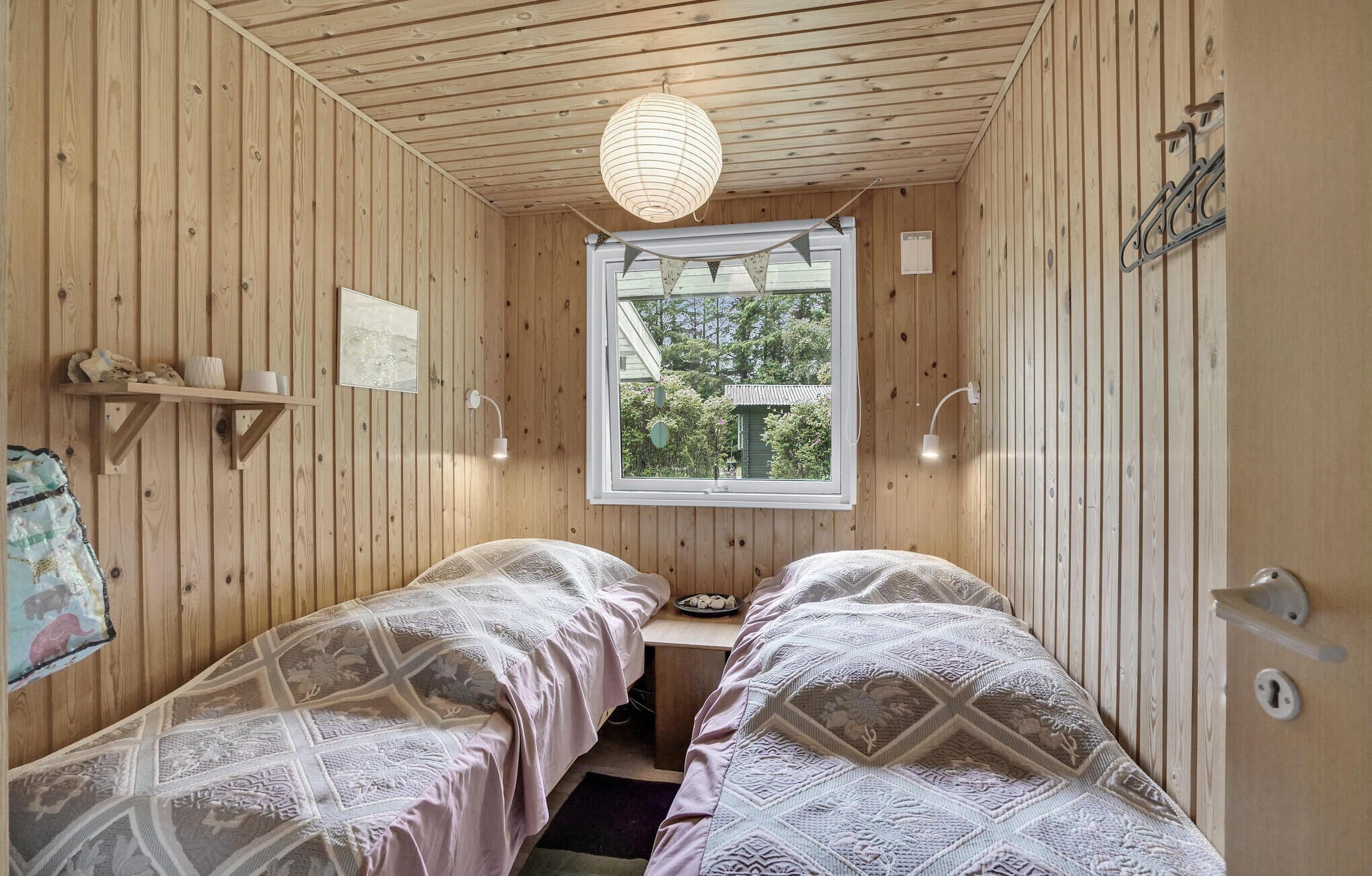 Una habitación de madera con dos camas, una ventana y una lámpara colgante.