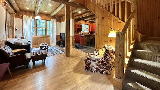Una amplia sala de estar con una escalera de madera, una chimenea acogedora y vistas a la cocina.