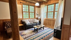 Un interior acogedor de cabaña con techo de madera, un sofá de cuero, una mesa de centro y una alfombra estampada.