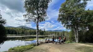 Un grupo de personas junto a un lago, con árboles y montañas al fondo.