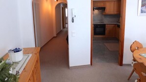 A hallway leading to a kitchen with wooden cabinets and a dining area with a table and chairs. - Charming apartment on the 1st floor, elevator, Entrée with wardrobe, living and  (Silvaplana-Surlej)