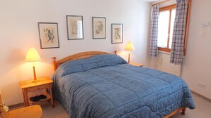 A bedroom with a large bed, two bedside tables with lamps, a wooden chair, and four framed botanical prints on the wall. - Charming apartment on the 1st floor, elevator, Entrée with wardrobe, living and  (Silvaplana-Surlej)